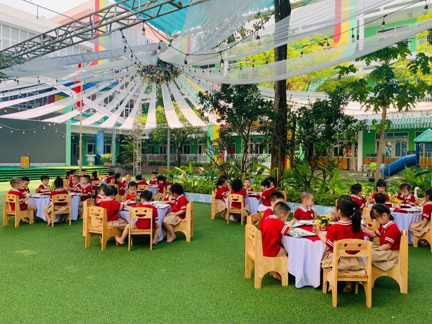 A group of children sitting at tables in a courtyard

Description automatically generated