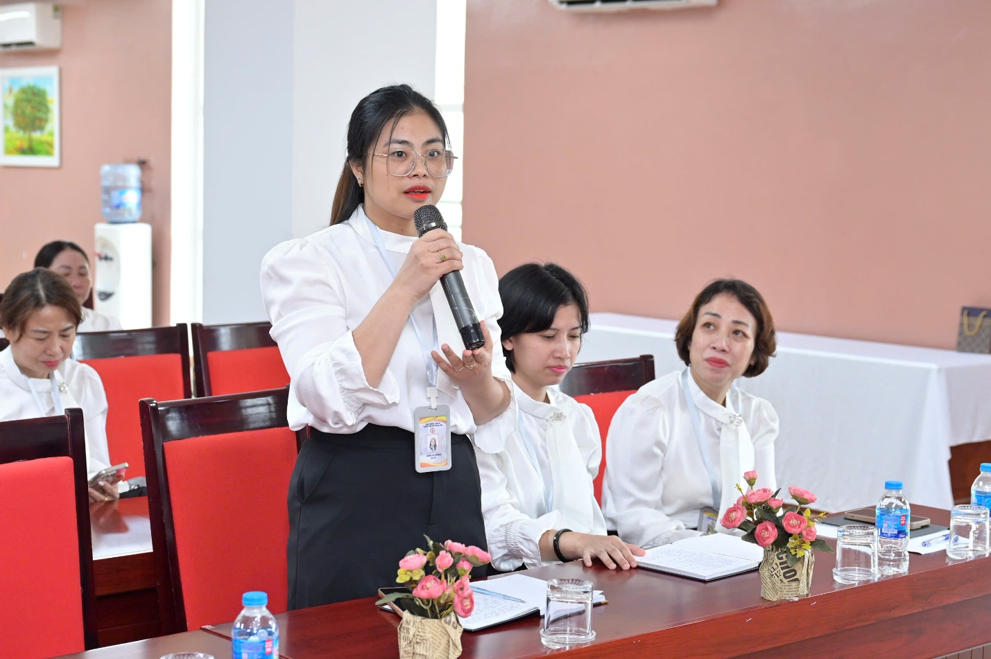 A person holding a microphone and standing next to a person sitting at a table

AI-generated content may be incorrect.