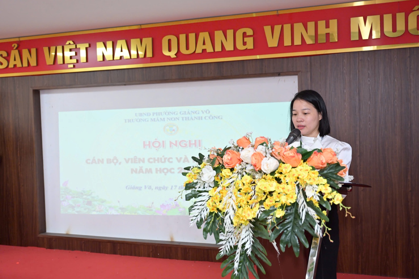 A person standing at a podium with flowers

AI-generated content may be incorrect.